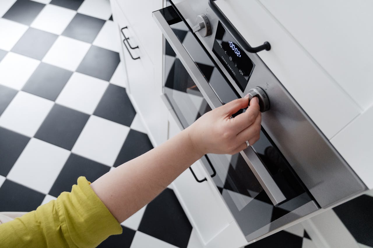 heros-img Hand adjusting the temperature dial on a modern stainless steel oven in a contemporary kitchen.